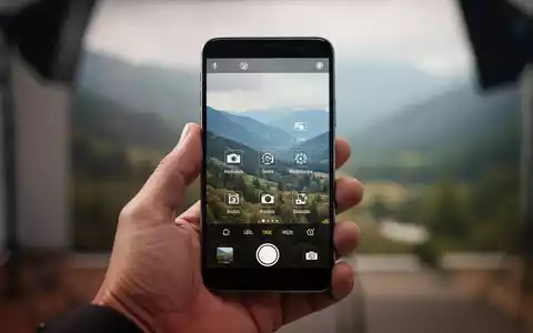 Eine Hand hält ein modernes Smartphone mit Kamera-App-Oberfläche, unscharfer Hintergrund deutet kreatives Umfeld an. - Foto: über boerse-global.de