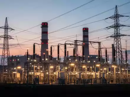 Eine Industrieanlage oder ein Kraftwerk bei Dämmerung, mit leuchtenden elektrischen Komponenten und Stromleitungen. - Foto: über boerse-global.de