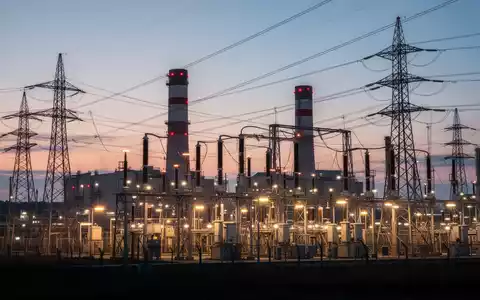 Eine Industrieanlage oder ein Kraftwerk bei Dämmerung, mit leuchtenden elektrischen Komponenten und Stromleitungen. - Foto: über boerse-global.de
