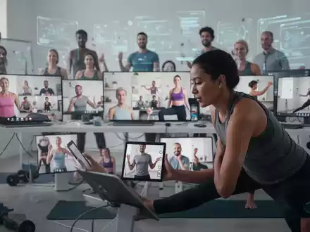 Eine Gruppe von Personen nimmt an einem Online-Fitnesskurs teil, sichtbar auf digitalen Bildschirmen in einem modernen Arbeitsumfeld. - Foto: über boerse-global.de