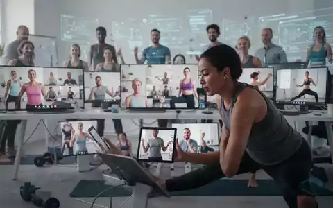 Eine Gruppe von Personen nimmt an einem Online-Fitnesskurs teil, sichtbar auf digitalen Bildschirmen in einem modernen Arbeitsumfeld. - Foto: über boerse-global.de