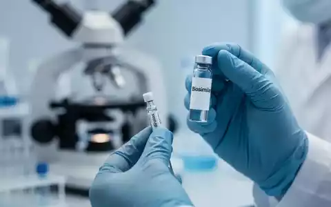 Hände eines Wissenschaftlers in einem Labor, der ein Biosimilar-Fläschchen hält, mit einem unscharfen Mikroskop im Hintergrund. - Foto: über boerse-global.de