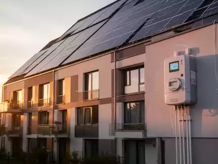Eine moderne Wohngebäude-Fassade mit Solarpaneelen und intelligenten Zählern, die Energie-Sharing und nachhaltige Heizlösungen symbolisiert. - Foto: über boerse-global.de