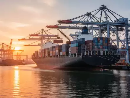 Ein geschäftiger Containerhafen bei Sonnenuntergang, mit einem großen Frachtschiff, das beladen wird, und Kränen im Hintergrund. - Foto: über boerse-global.de