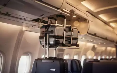 Ein Handgepäckkoffer wird in das Gepäckfach eines modernen Flugzeugs geschoben, um die neuen EU-Regeln zu illustrieren. - Foto: über boerse-global.de