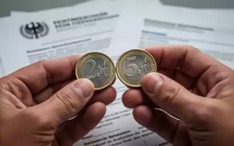 Hände halten deutsche Euromünzen, die die Prozentsätze 2% und 5% symbolisieren, vor verschwommenen Regierungsdokumenten. - Foto: über boerse-global.de