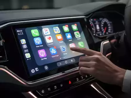 Modernes Auto-Armaturenbrett mit Apple CarPlay-Oberfläche und App-Symbolen, beleuchtet durch sanftes Umgebungslicht. - Foto: über boerse-global.de