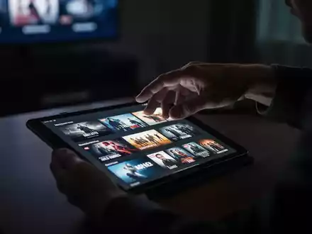 Eine Hand schwebt über einem Tablet, das zahlreiche Streaming-Optionen anzeigt, was Entscheidungsmüdigkeit symbolisiert. - Foto: über boerse-global.de