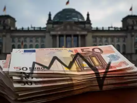 Nahaufnahme von Euro-Banknoten mit dem Schatten eines fallenden Diagramms und einem unscharfen deutschen Parlamentsgebäude im Hintergrund. - Foto: über boerse-global.de