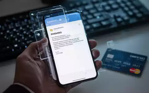Eine Hand hält ein Smartphone mit einer Phishing-E-Mail, im Hintergrund eine Tastatur und Kreditkarte, die Cyberbetrug symbolisieren. - Foto: über boerse-global.de
