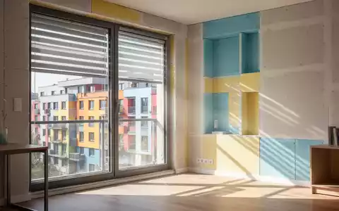 Ein modernes Apartment-Interieur an einem heißen Tag, mit sichtbaren Außenbeschattungssystemen und hellem Tageslicht, das auf einen kühlen Raum fällt. - Foto: über boerse-global.de