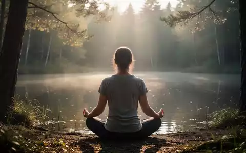 Eine Person sitzt in meditativer Haltung in einer ruhigen Naturlandschaft, umgeben von Bäumen und weichem Licht. - Foto: über boerse-global.de