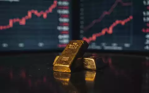 Ein glänzender Goldbarren liegt auf einer dunklen Oberfläche, umgeben von verschwommenen digitalen Börsenkursen, die einen Abwärtstrend zeigen. - Foto: über boerse-global.de