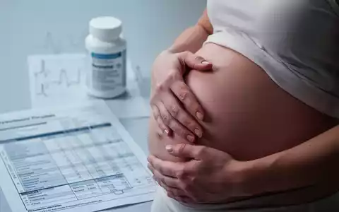 Nahaufnahme der Hand einer schwangeren Frau auf ihrem Bauch, mit verschwommenen medizinischen Elementen im Hintergrund. - Foto: über boerse-global.de
