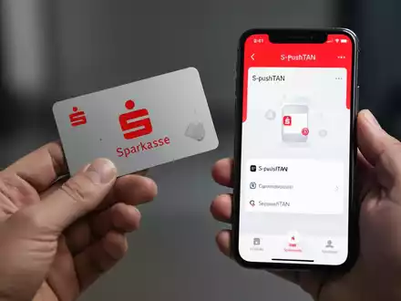 Eine Hand hält eine Sparkassen-Bankkarte mit neuem Design neben einem Smartphone, das die S-pushTAN-App anzeigt, symbolisch für digitale Zahlungsänderungen. - Foto: über boerse-global.de