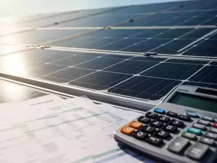 Nahaufnahme eines Solarpark-Moduls mit unscharfen Finanzdokumenten und einem Taschenrechner im Vordergrund, der Investitionen und Steuerplanung symbolisiert. - Foto: über boerse-global.de