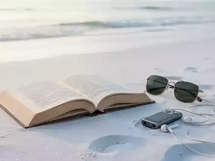 Ein offenes Buch, Sonnenbrille und Kopfhörer liegen auf sauberem, weißem Sand am Strand, minimalistische Urlaubsszene. - Foto: über boerse-global.de
