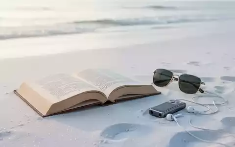 Ein offenes Buch, Sonnenbrille und Kopfhörer liegen auf sauberem, weißem Sand am Strand, minimalistische Urlaubsszene. - Foto: über boerse-global.de