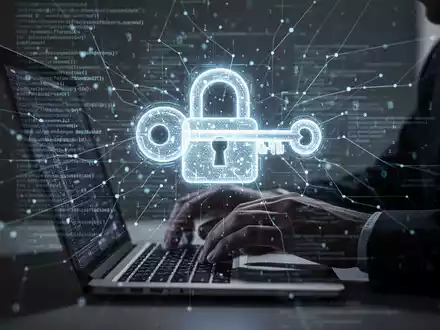 Schattenhafte Hände tippen auf Laptop, Bildschirm zeigt leuchtendes Schloss- und Schlüsselsymbol für digitale Sicherheitsbedrohung. - Foto: über boerse-global.de