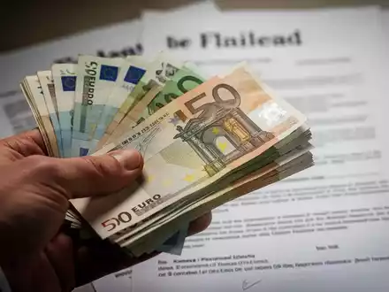 Eine Hand hält einen Stapel Euro-Banknoten, im Hintergrund verschwommen ein juristisches Dokument oder Testament. - Foto: über boerse-global.de