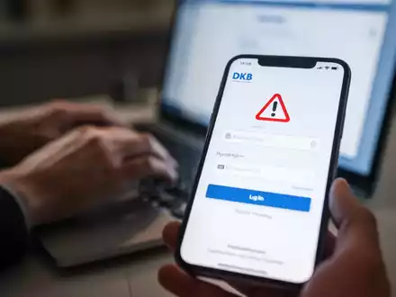 Smartphone mit gefälschter DKB-Loginseite, unscharfe Hände tippen im Hintergrund auf Laptop, Phishing-Betrug. - Foto: über boerse-global.de