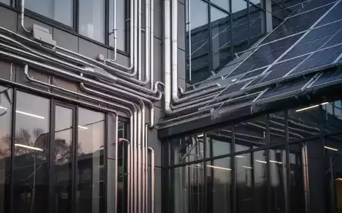 Ein modernes Gebäude mit sichtbaren Heizungsrohren und Solaranlagen, das traditionelle und erneuerbare Energien symbolisiert. - Foto: über boerse-global.de