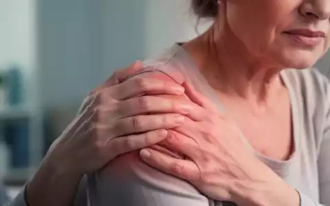Eine Frau hält ihre schmerzende Schulter, die Hände leicht auf den Gelenkbereich gelegt, was auf Unbehagen hinweist. - Foto: über boerse-global.de