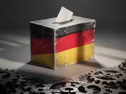 Eine stilisierte, abstrakte Wahlurne mit einem subtilen, gealterten Motiv der deutschen Flagge und Zahnrädern im Vordergrund. - Foto: über boerse-global.de