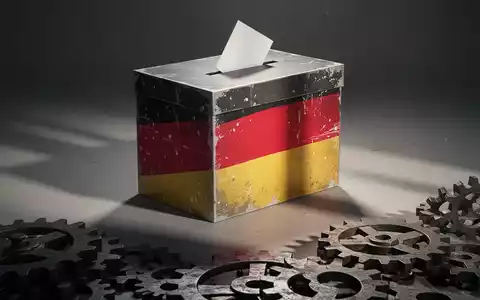 Eine stilisierte, abstrakte Wahlurne mit einem subtilen, gealterten Motiv der deutschen Flagge und Zahnrädern im Vordergrund. - Foto: über boerse-global.de