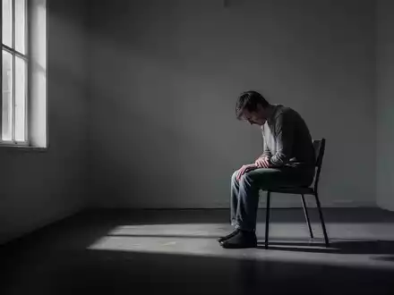 Eine einzelne Person sitzt in einem spärlich beleuchteten Raum, was Gefühle von Isolation und Kampf symbolisiert. - Foto: über boerse-global.de