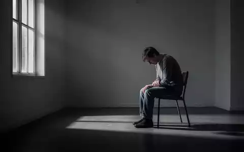Eine einzelne Person sitzt in einem spärlich beleuchteten Raum, was Gefühle von Isolation und Kampf symbolisiert. - Foto: über boerse-global.de
