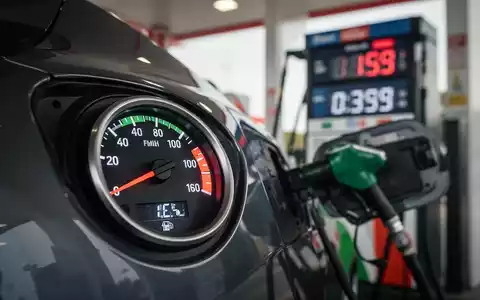 Nahaufnahme einer Tankanzeige, die einen vollen Tank anzeigt, mit einer unscharfen Tankstelle im Hintergrund. - Foto: über boerse-global.de