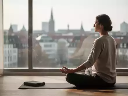 Eine Person meditiert in einem ruhigen Raum mit Blick auf die Stadt Hannover, um Entspannung und Stressbewältigung darzustellen. - Foto: über boerse-global.de