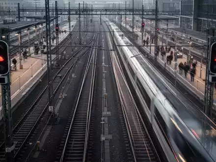 Mehrere sich kreuzende Bahngleise an einem geschäftigen deutschen Bahnhof mit einem durchfahrenden Hochgeschwindigkeitszug. - Foto: über boerse-global.de