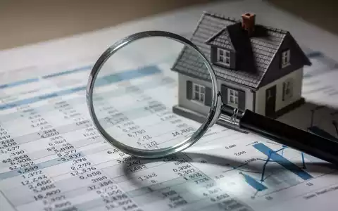 Eine Lupe vergrößert einen Finanzbericht mit Zahlen und Diagrammen, hinter der ein kleines Hausmodell steht, um die Prüfung von Immobilienwerten darzustellen. - Foto: über boerse-global.de
