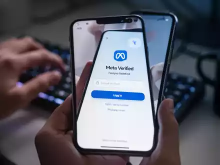 Ein Smartphone zeigt eine gefälschte Meta-Verified-Anmeldeseite, im Hintergrund unscharfe Hände auf einer Tastatur. - Foto: über boerse-global.de