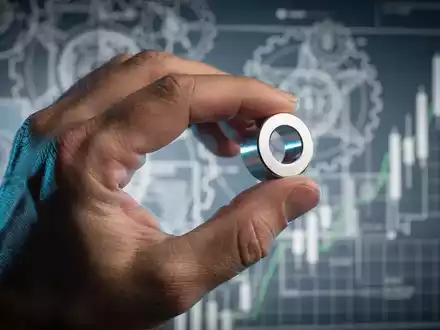 Nahaufnahme einer Hand, die einen seltenen Erdmagneten hält, mit verschwommenen Industrieschemata und Finanzdiagrammen im Hintergrund. - Foto: über boerse-global.de