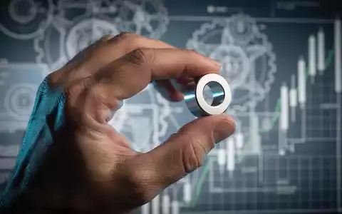 Nahaufnahme einer Hand, die einen seltenen Erdmagneten hält, mit verschwommenen Industrieschemata und Finanzdiagrammen im Hintergrund. - Foto: über boerse-global.de