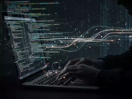Hände tippen auf einer beleuchteten Tastatur, während leuchtende Datenströme über den Bildschirm fließen, symbolisieren Online-Betrug und KI. - Foto: über boerse-global.de