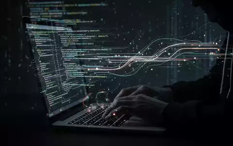 Hände tippen auf einer beleuchteten Tastatur, während leuchtende Datenströme über den Bildschirm fließen, symbolisieren Online-Betrug und KI. - Foto: über boerse-global.de