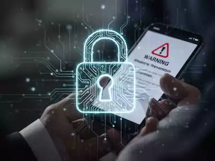 Ein stilisiertes digitales Vorhängeschloss-Symbol mit leuchtenden Schaltkreisen über einer Person, die ein Smartphone mit einer Warnmeldung hält. - Foto: über boerse-global.de