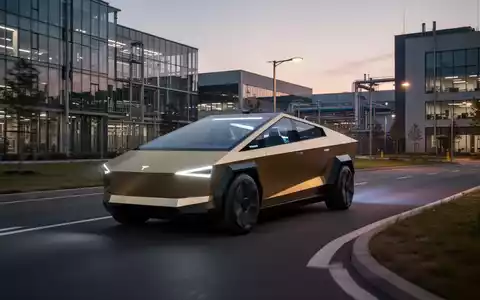 Goldenes Tesla Cybercab, autonomes Fahrzeug ohne Lenkrad, fährt in der Dämmerung auf einer Straße durch einen modernen Fabrikcampus. - Foto: über boerse-global.de