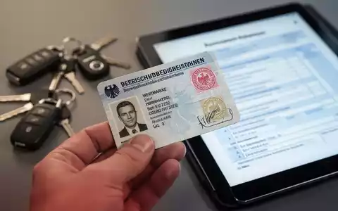 Nahaufnahme eines Schwerbehindertenausweises mit Wertmarke, gehalten von einer Hand, im Hintergrund unscharf Autoschlüssel und Tablet. - Foto: über boerse-global.de