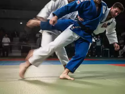 Ein Judoka in blauem Judogi führt eine dynamische Bewegung auf einer Tatami-Matte aus, die Kniestabilität und Kontrolle betont. - Foto: über boerse-global.de