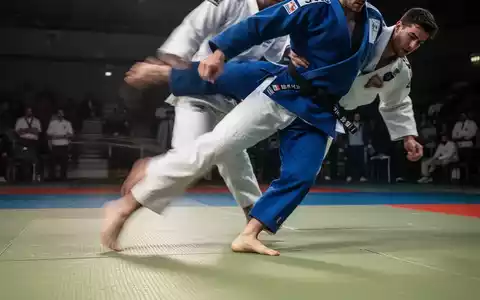 Ein Judoka in blauem Judogi führt eine dynamische Bewegung auf einer Tatami-Matte aus, die Kniestabilität und Kontrolle betont. - Foto: über boerse-global.de