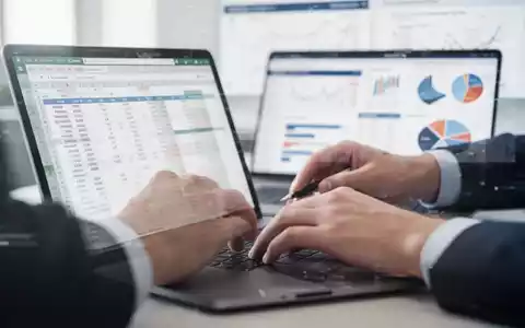 Nahaufnahme von Händen, die an einer Laptop-Tabelle arbeiten, mit verschwommenen Finanzdaten im Hintergrund, symbolisiert Excel-Kenntnisse. - Foto: über boerse-global.de
