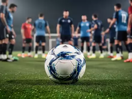 Ein Fußball liegt auf einem grünen Rasen, im Hintergrund verschwommene Fußballspieler beim Training. - Foto: über boerse-global.de