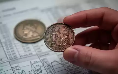 Nahaufnahme einer Hand, die eine britische Penny-Münze hält, mit einer weiteren Münze im Hintergrund, die kleine finanzielle Differenzen symbolisiert. - Foto: über boerse-global.de