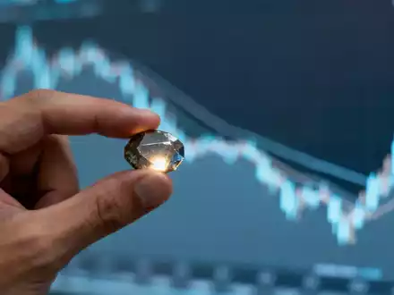 Eine Hand hält ein seltenes Erdmineral vor einem leicht fallenden digitalen Börsenchart. - Foto: über boerse-global.de