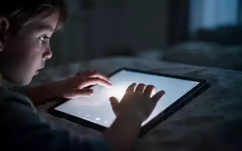 Hände eines Kindes, die nach einem leuchtenden Tablet-Bildschirm in einem dunklen Raum greifen, was digitale Nutzung symbolisiert. - Foto: über boerse-global.de